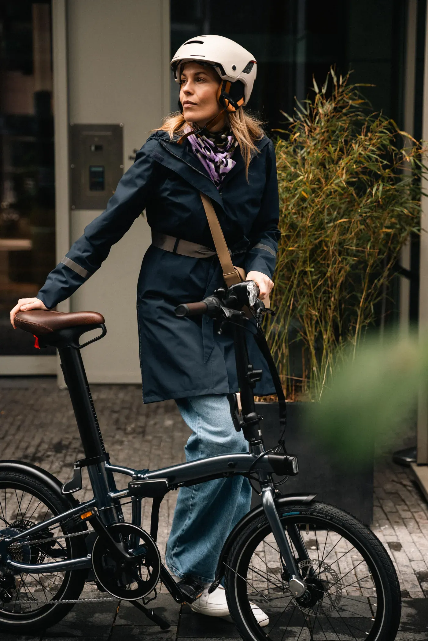 Cycliste en imperméable tenant un Decathlon E-Fold 900 déplié devant un immeuble