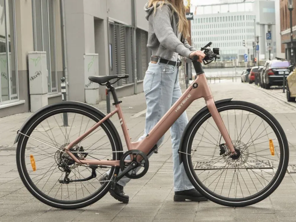 Une cycliste tient par le guidon un Heybike EC 1-ST rose sur un trottoir pavé en ville